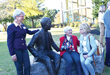 Three women sitting and standing next to a statue. Links to Gifts by Estate Note